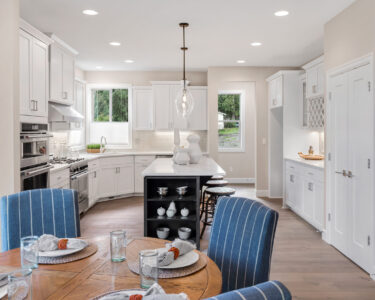 Kitchen and dining area in new luxury home. Features kitchen island, table with place settings, stainless steel appliances, and pendant lights.